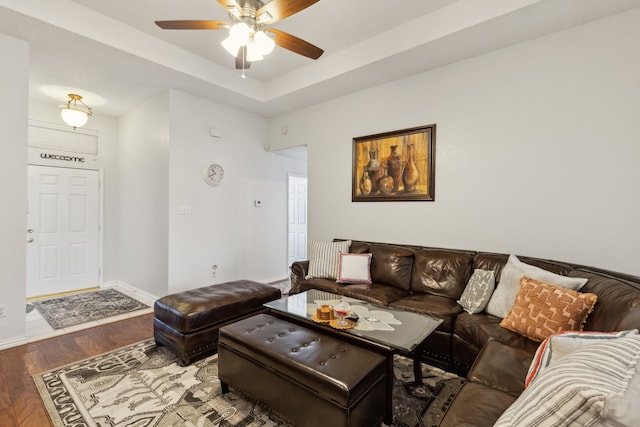 living area with a tray ceiling, ceiling fan, baseboards, and wood finished floors