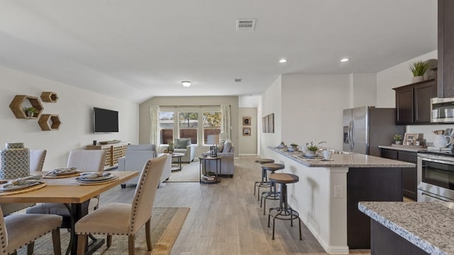 kitchen with a breakfast bar area, stainless steel appliances, visible vents, open floor plan, and dark brown cabinetry