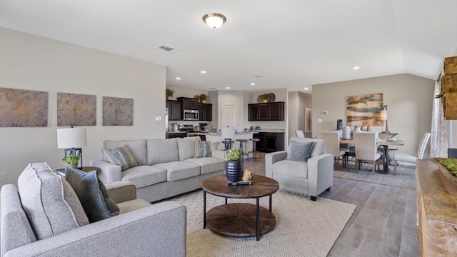 living area featuring light wood-style floors, recessed lighting, visible vents, and vaulted ceiling