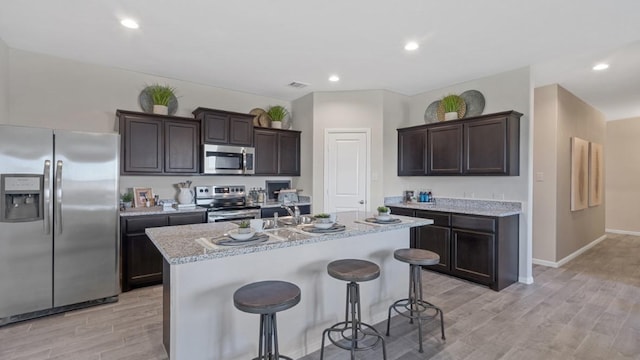 kitchen with light wood-style flooring, dark brown cabinetry, a breakfast bar, appliances with stainless steel finishes, and an island with sink