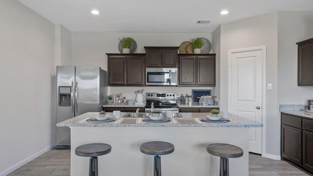 kitchen with dark brown cabinetry, visible vents, appliances with stainless steel finishes, a kitchen bar, and a center island with sink