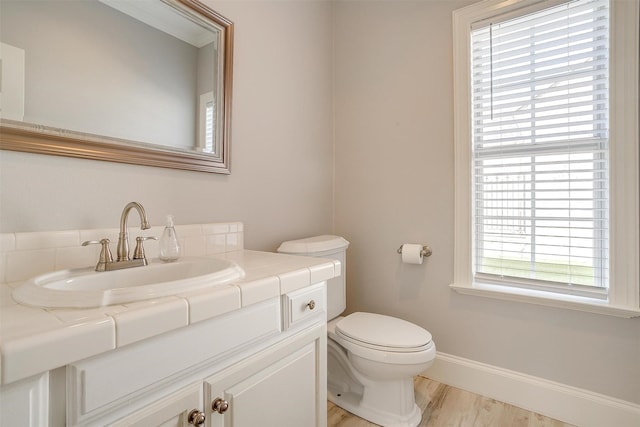 half bathroom with toilet, baseboards, wood finished floors, and vanity