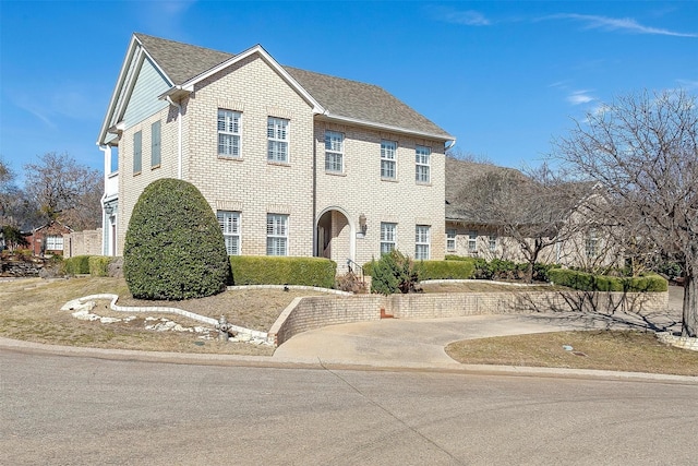 view of front of house with concrete driveway, brick siding, and a shingled roof