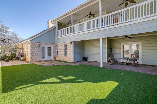 back of property with ceiling fan, brick siding, a yard, french doors, and a patio area