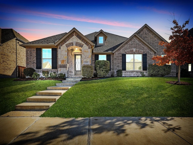 french country style house with stone siding, brick siding, and a front yard