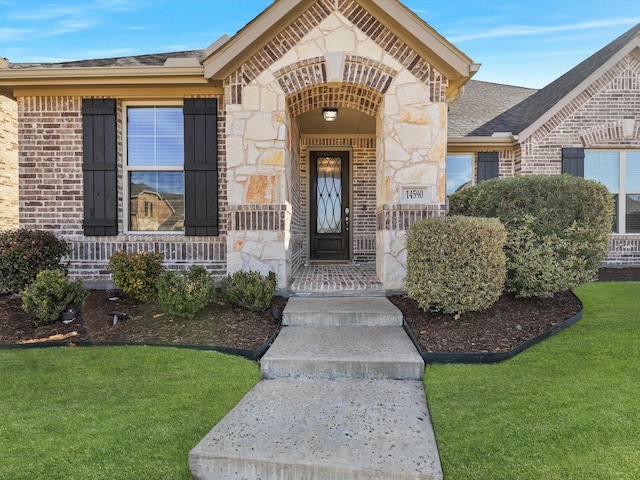 doorway to property with covered porch, brick siding, stone siding, a lawn, and roof with shingles