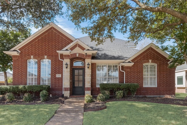 view of front facade with a shingled roof, a front yard, and brick siding