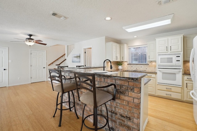 kitchen featuring a breakfast bar area, light wood finished floors, visible vents, decorative backsplash, and white appliances