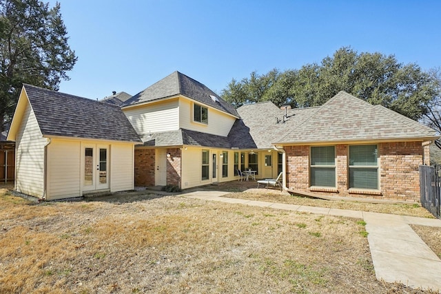 rear view of house featuring a shingled roof, french doors, brick siding, and a yard