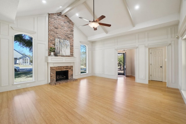 unfurnished living room featuring high vaulted ceiling, light wood-style flooring, a decorative wall, a fireplace, and beamed ceiling