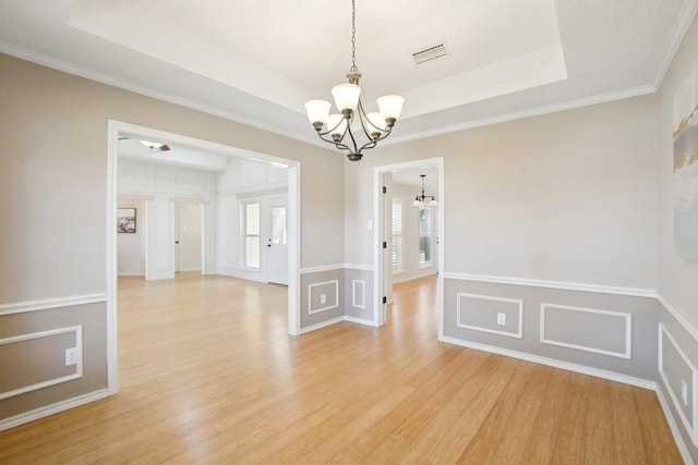 empty room featuring light wood finished floors, visible vents, a raised ceiling, and an inviting chandelier