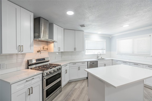 kitchen featuring stainless steel appliances, visible vents, light wood-type flooring, wall chimney exhaust hood, and tasteful backsplash