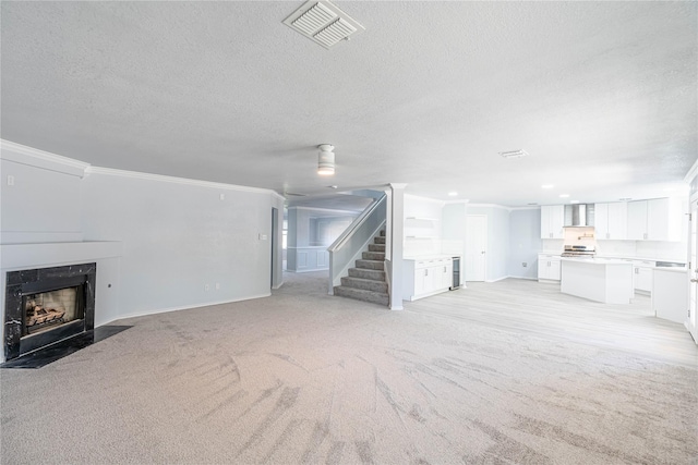 unfurnished living room with a textured ceiling, a premium fireplace, visible vents, stairs, and crown molding