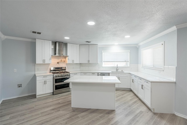 kitchen featuring range with two ovens, light wood-style flooring, a sink, visible vents, and wall chimney exhaust hood