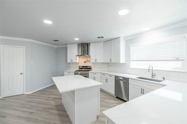 kitchen featuring visible vents, a center island, stainless steel appliances, wall chimney range hood, and a sink