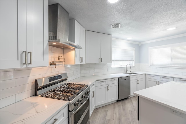 kitchen featuring visible vents, decorative backsplash, wall chimney exhaust hood, appliances with stainless steel finishes, and a sink