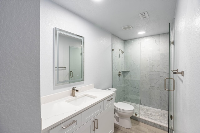 bathroom with a marble finish shower, visible vents, toilet, wood finished floors, and vanity