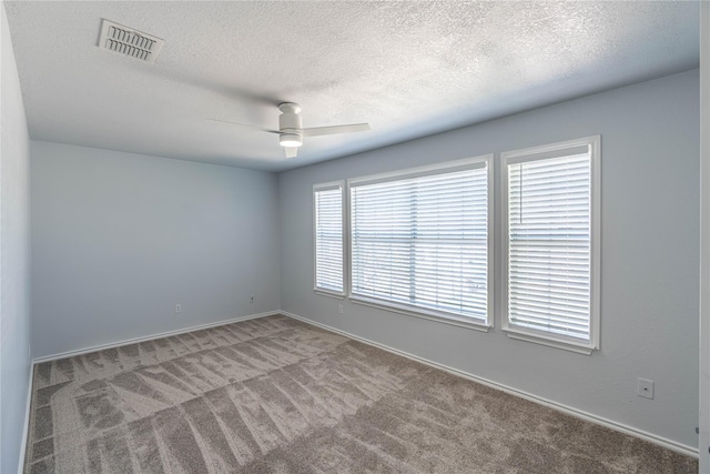 carpeted empty room featuring baseboards, ceiling fan, visible vents, and a textured ceiling