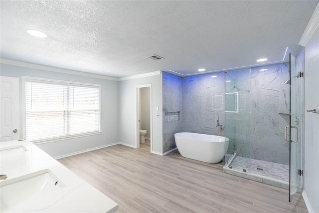 bathroom featuring a textured ceiling, a sink, wood finished floors, visible vents, and a marble finish shower