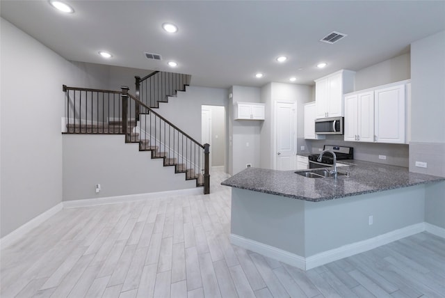 kitchen with light wood finished floors, visible vents, stainless steel microwave, a sink, and dark stone countertops