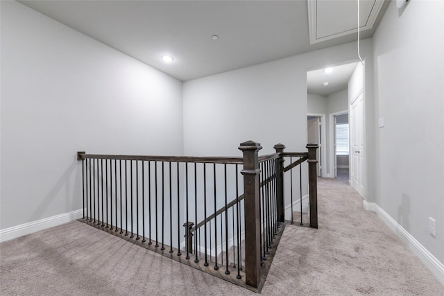 hallway featuring attic access, baseboards, carpet flooring, and an upstairs landing