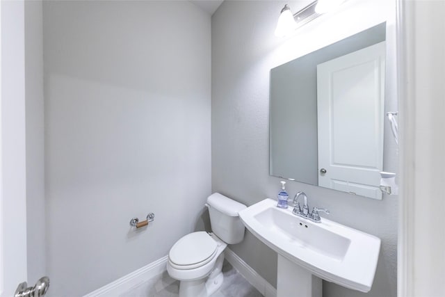 half bathroom with a sink, toilet, and baseboards