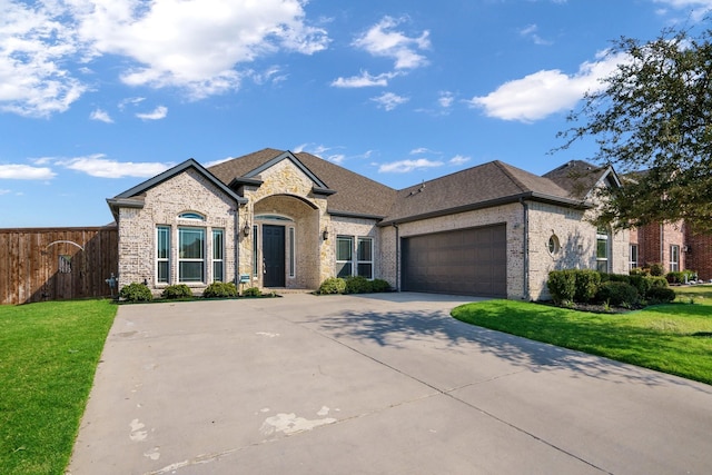 french country home with a garage, brick siding, a front yard, and fence