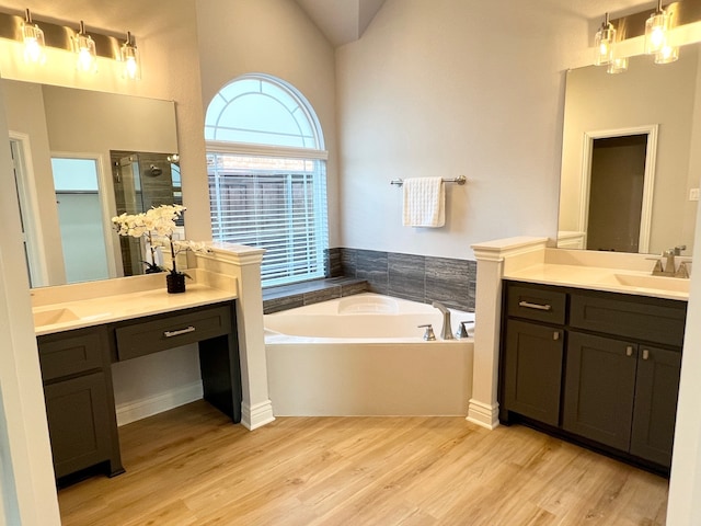 bathroom featuring wood finished floors, a sink, vaulted ceiling, a bath, and a stall shower