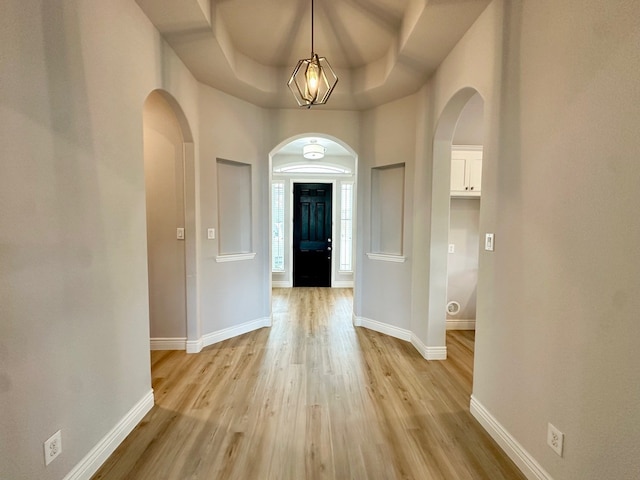 foyer entrance with baseboards, a tray ceiling, arched walkways, and light wood-style floors