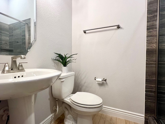 bathroom featuring toilet, a sink, a shower stall, wood finished floors, and baseboards