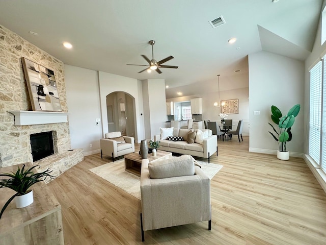 living room with light wood-style floors, visible vents, arched walkways, and a stone fireplace