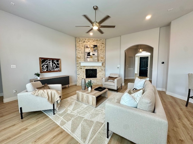 living room with light wood finished floors, a fireplace, arched walkways, and a ceiling fan