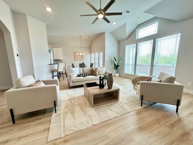 living area featuring arched walkways, high vaulted ceiling, light wood-style flooring, visible vents, and baseboards