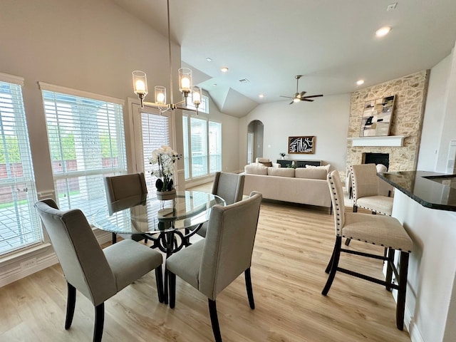 dining room featuring light wood-style flooring, arched walkways, vaulted ceiling, and a stone fireplace