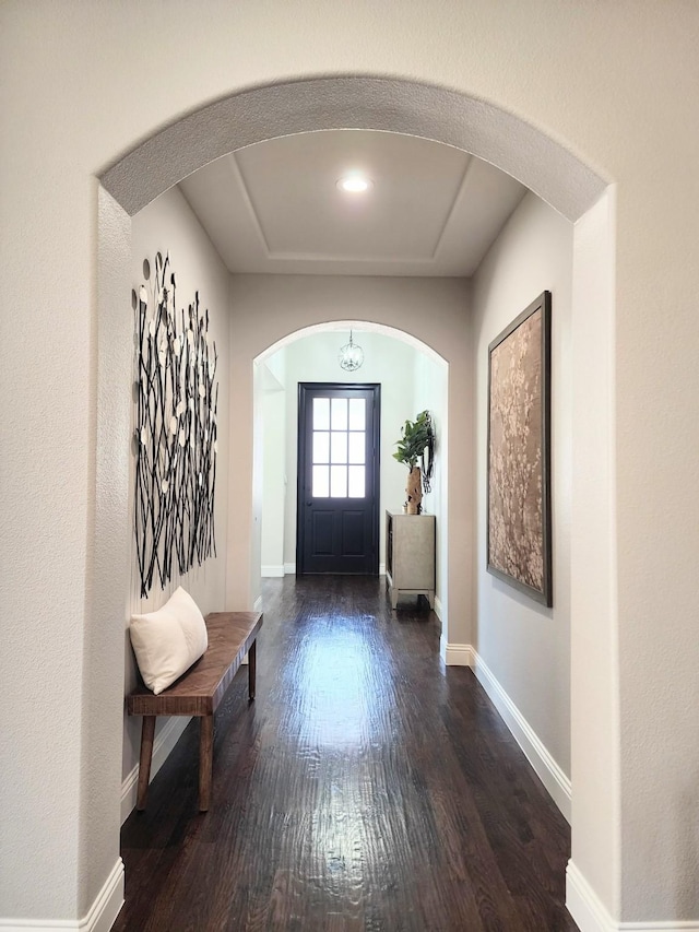 foyer entrance with baseboards, arched walkways, and wood finished floors