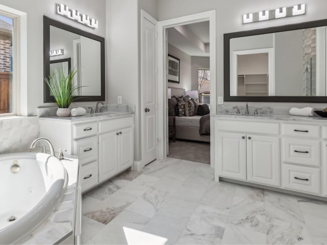 ensuite bathroom with two vanities, marble finish floor, a sink, and a tub with jets