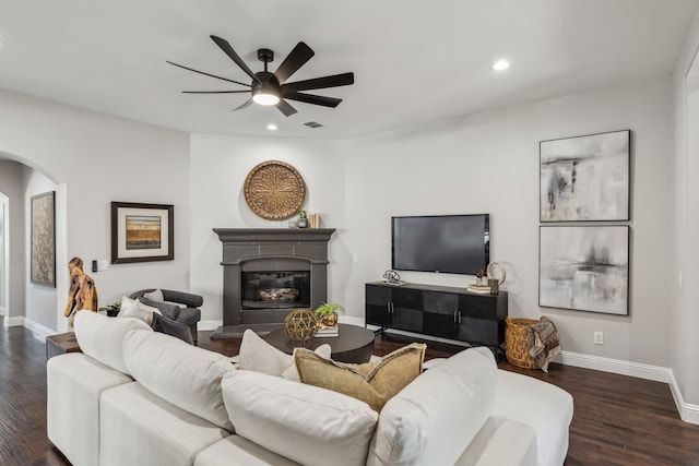 living room with baseboards, arched walkways, a glass covered fireplace, dark wood-type flooring, and recessed lighting