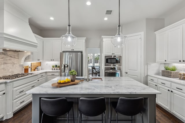 kitchen featuring an island with sink, premium range hood, white cabinetry, visible vents, and stainless steel appliances