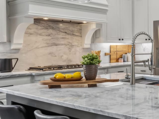 kitchen featuring light stone countertops, white cabinets, stainless steel gas cooktop, a sink, and decorative backsplash