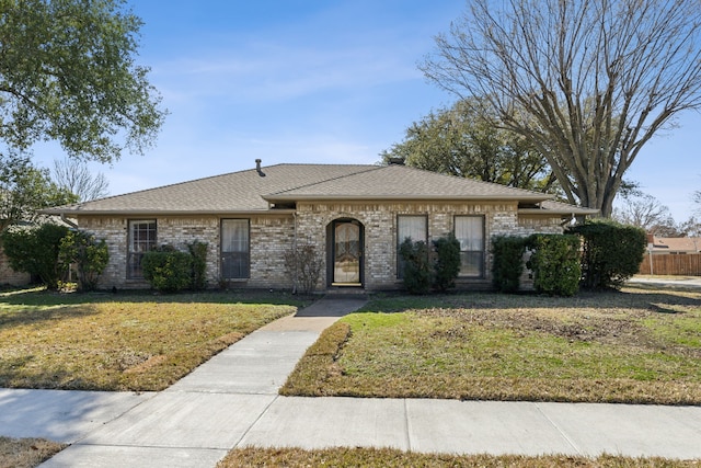 view of front of property with a shingled roof, a front yard, and brick siding