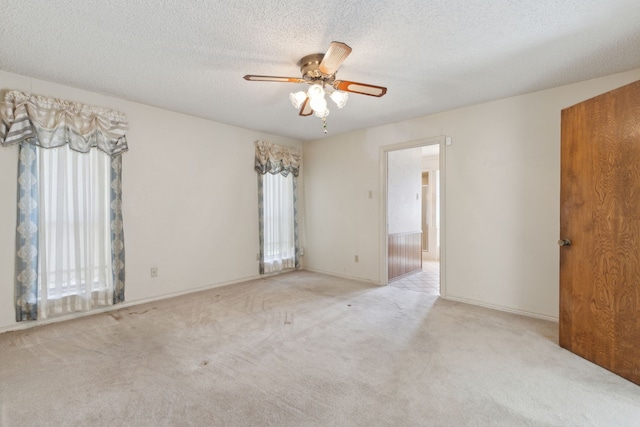 carpeted spare room featuring a textured ceiling, a ceiling fan, and baseboards