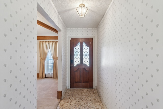 entrance foyer featuring a textured ceiling, baseboards, light colored carpet, and wallpapered walls