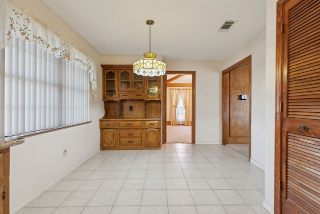 unfurnished dining area featuring visible vents, a textured ceiling, baseboards, and light tile patterned floors