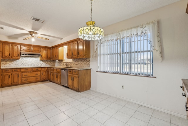 kitchen featuring under cabinet range hood, visible vents, stainless steel dishwasher, brown cabinets, and decorative backsplash