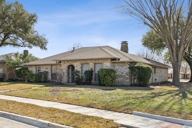 view of front of property featuring roof with shingles, a front lawn, a chimney, and brick siding