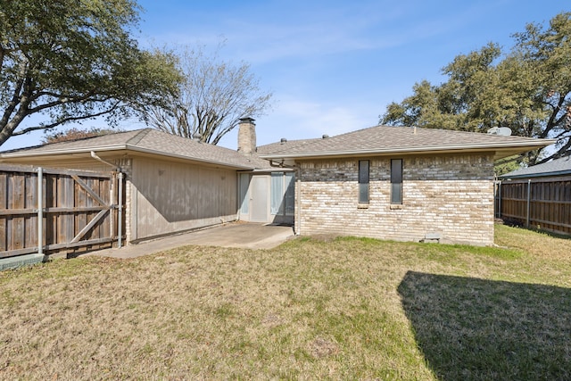 rear view of property with a yard, brick siding, fence, and a chimney