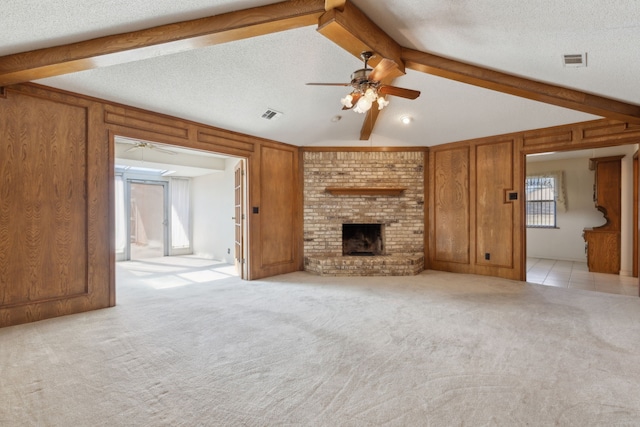 unfurnished living room with a textured ceiling, light carpet, wood walls, visible vents, and a brick fireplace