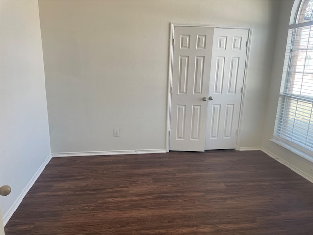 unfurnished bedroom with a closet, baseboards, and dark wood-type flooring