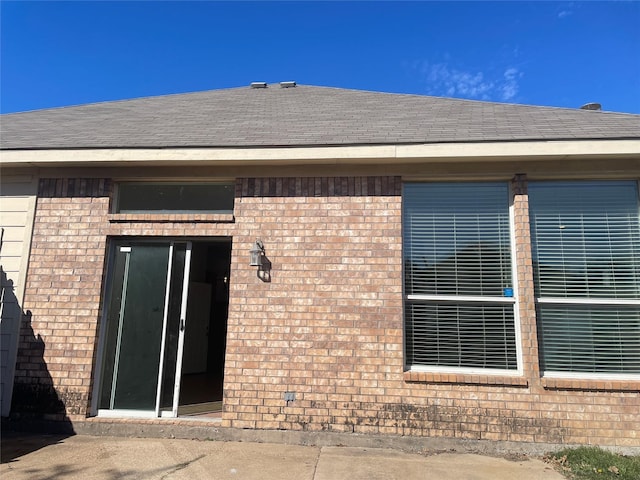 view of home's exterior with brick siding and roof with shingles