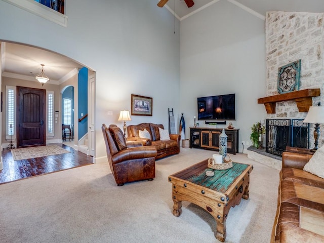 carpeted living area featuring arched walkways, high vaulted ceiling, ornamental molding, and a stone fireplace